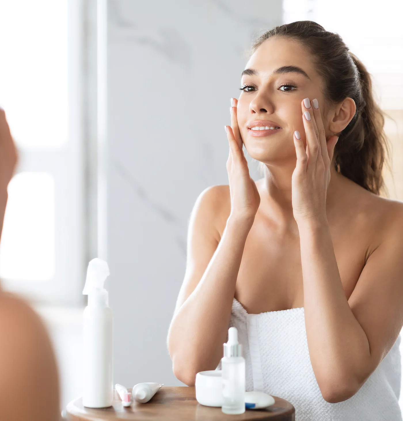 woman looking in mirror and applying skincare product to her face